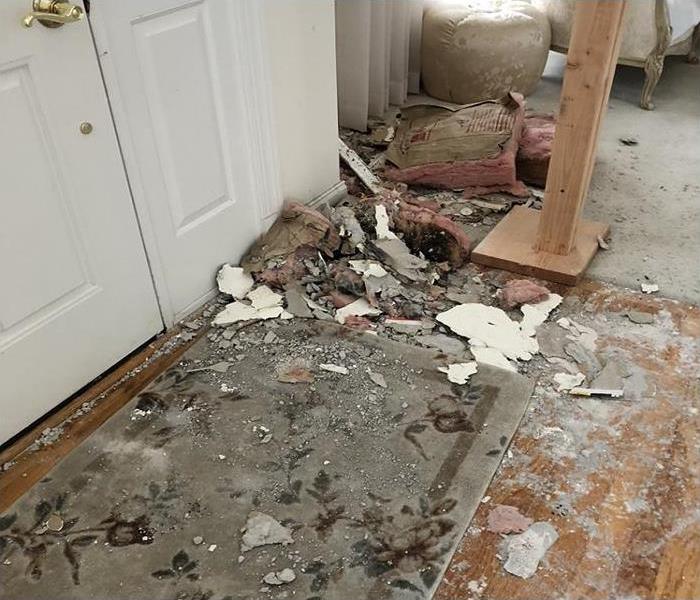 The hardwood floor of a foyer covered in burned insulation, sheet rock, soot and debris