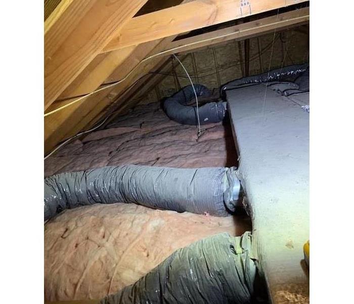 Soot and smoke covered rafters and ductwork in an attic