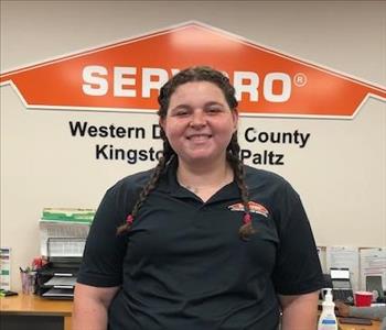 A photo of a smiling female SERVPRO employee with long brown braids in a black SERVPRO sweater