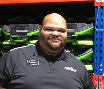 A photo of a smiling male employee wearing a black SERVPRO shirt standing in front of green SERVPRO equipment