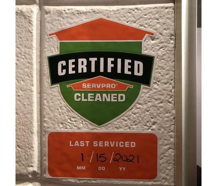 A painted white cement wall with the Certified: SERVPRO Cleaned shield and date serviced sticker displayed.