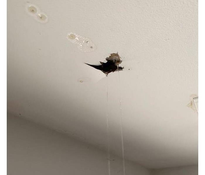 A photo of a white ceiling with a large crack and hole in it with a stream of water flowing out to the floor.