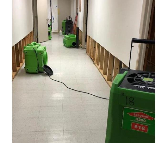 Multiple pieces of green SERVPRO drying equipment placed throughout a white hallway in a commercial building