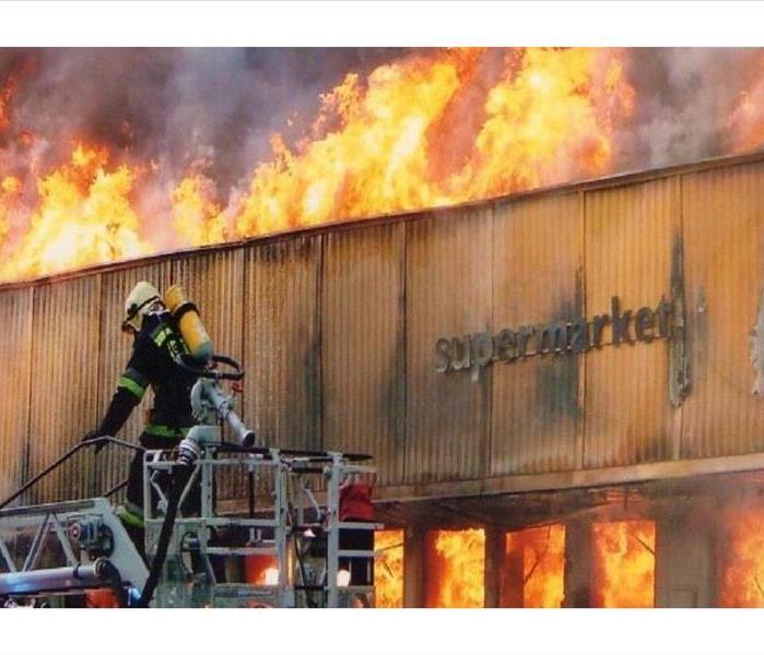 A photo of the exterior of a supermarket engulfed in flames while firefighters try to battle it.