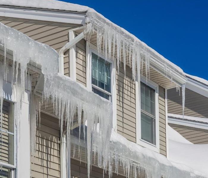 The upper portion of a white house loaded with icicles and accumulated snow on the roof and eaves.