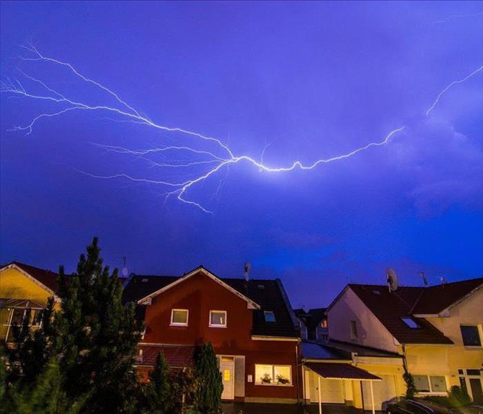 A bolt of lightning striking over a row of homes against a dark blue sky