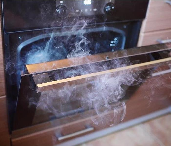 A partially opened oven filled with smoke 