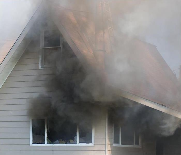 Black smoke coming out of broken windows in a burning house
