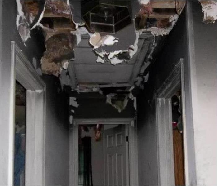 A blackened, collapsing ceiling in the hallway of a home with gutted and burned from an electrical fire above