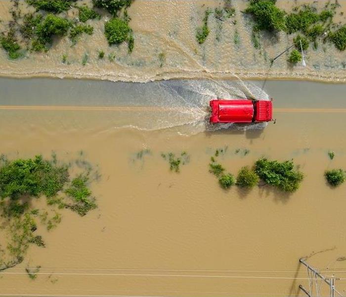 An aerial view of a red truck truck driving through dirty flooded roads
