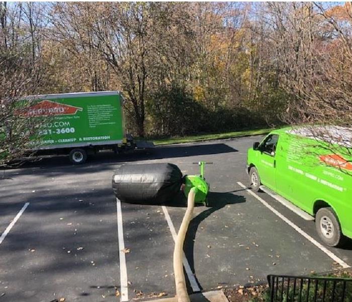 A photo of 2 green SERVPRO trucks in a parking lot with an insulation vacuum and full bag attached.