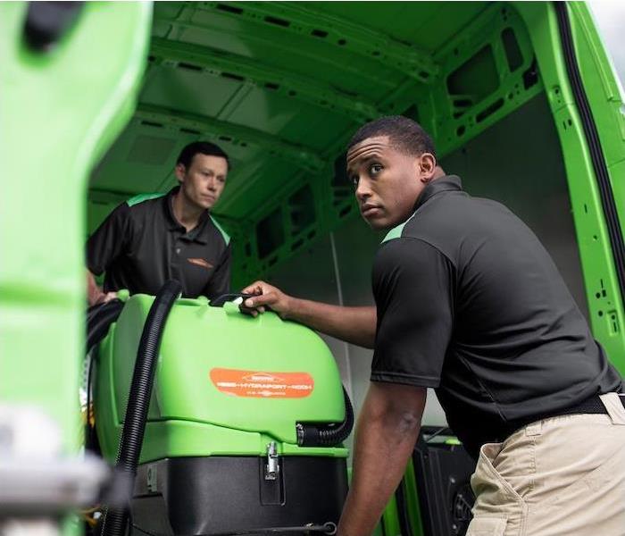 2 SERVPRO employees maneuvering equipment out of a green SERVPRO truck.
