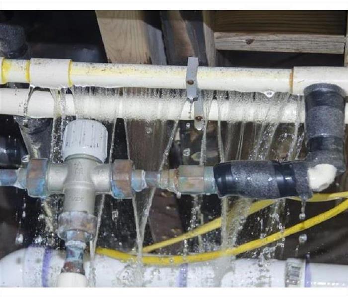 A cluster of frozen, white pvc pipes and steel pipes forcefully leaking water.