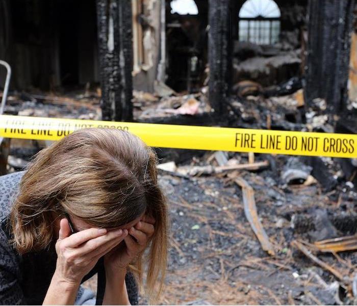 woman with hands covering face upset with burnt house in background